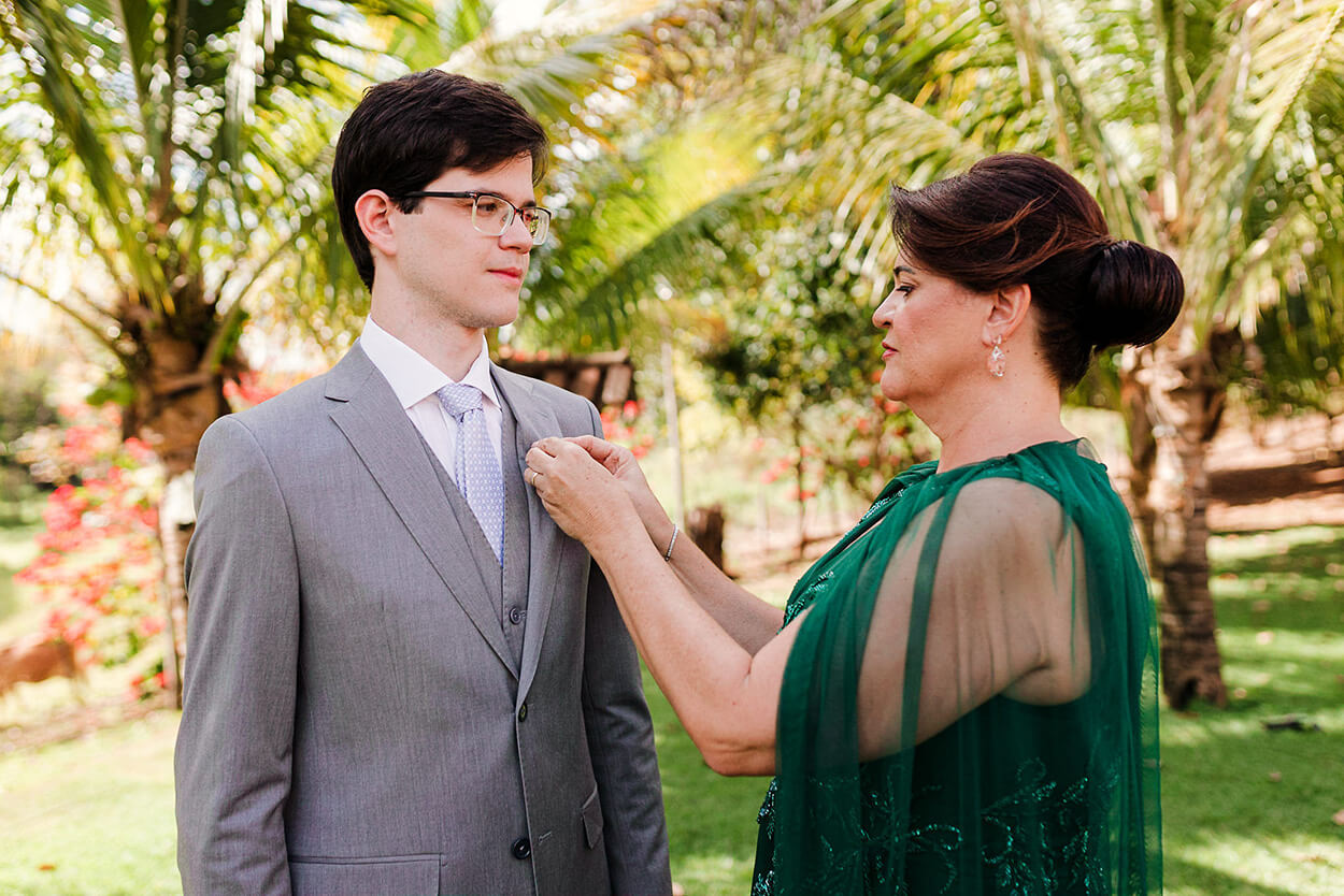 mãe da noiva com vestido verde ajustando terno cinza