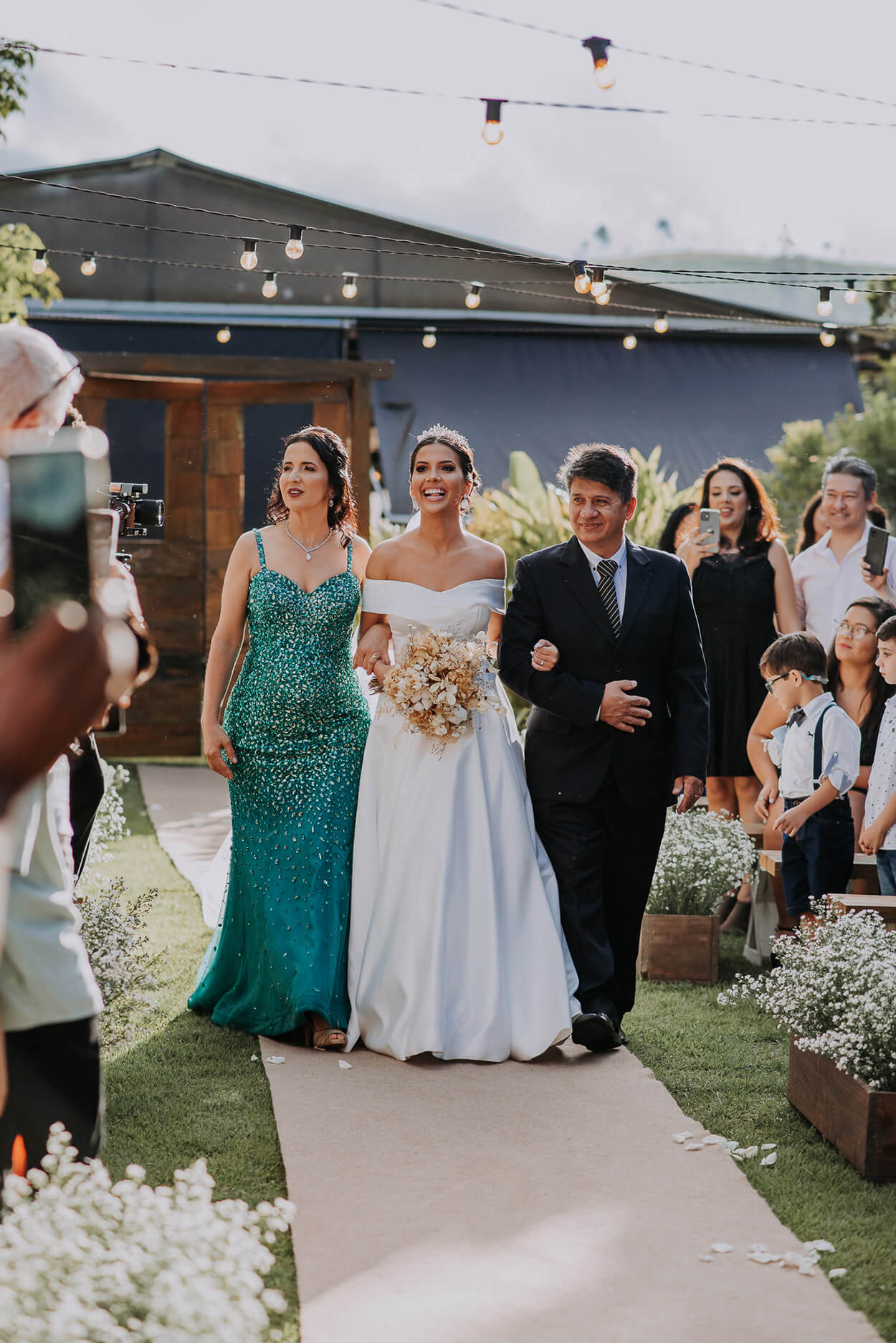 entrada da noiva ao lado do pai com terno preto e mãe com vestido verde brilhante