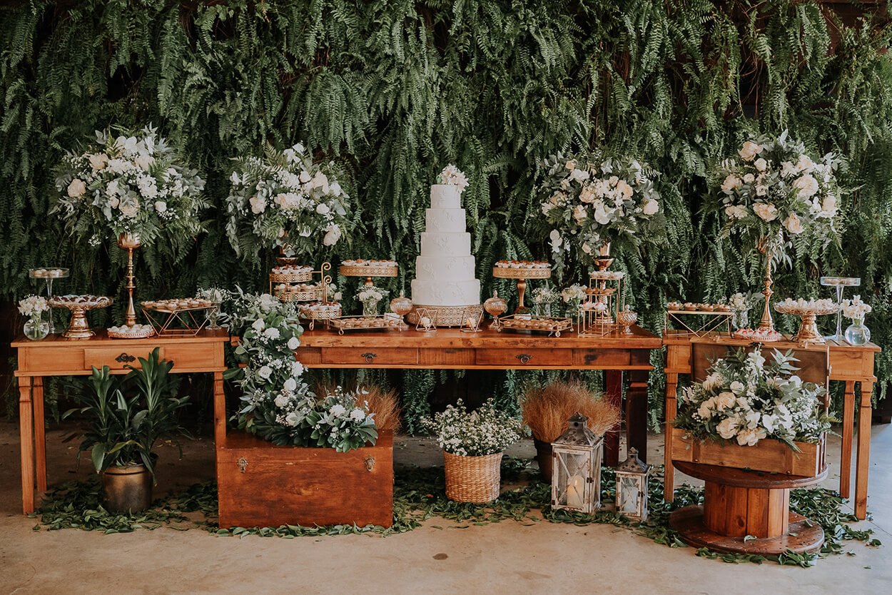mesas de madeira com bolo de casamento branco com cinco andares com vasos com flores brancas