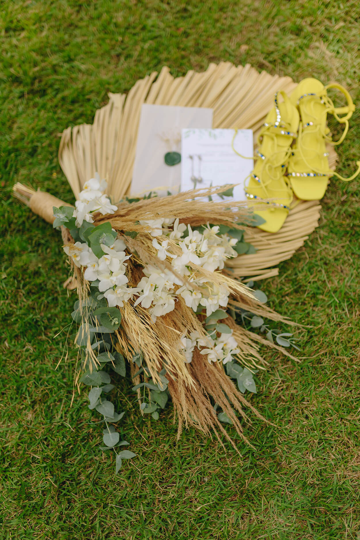 buquê com capim dos pampas e flores brancas ao lado do convite de casamento com sandalia amarela
