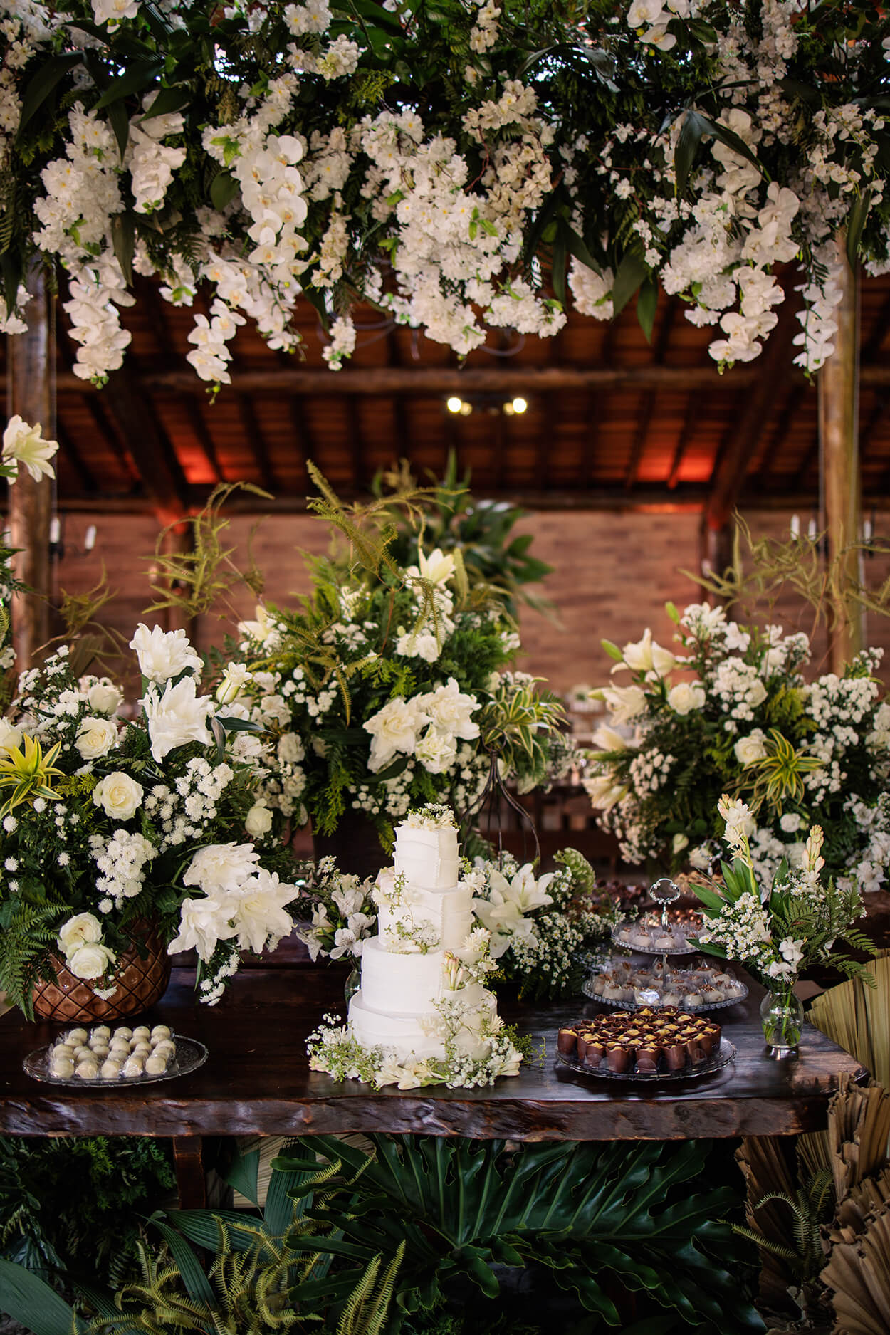salão rústico com mesa com doces de casamento e bolo de casamento branco com quatro andares