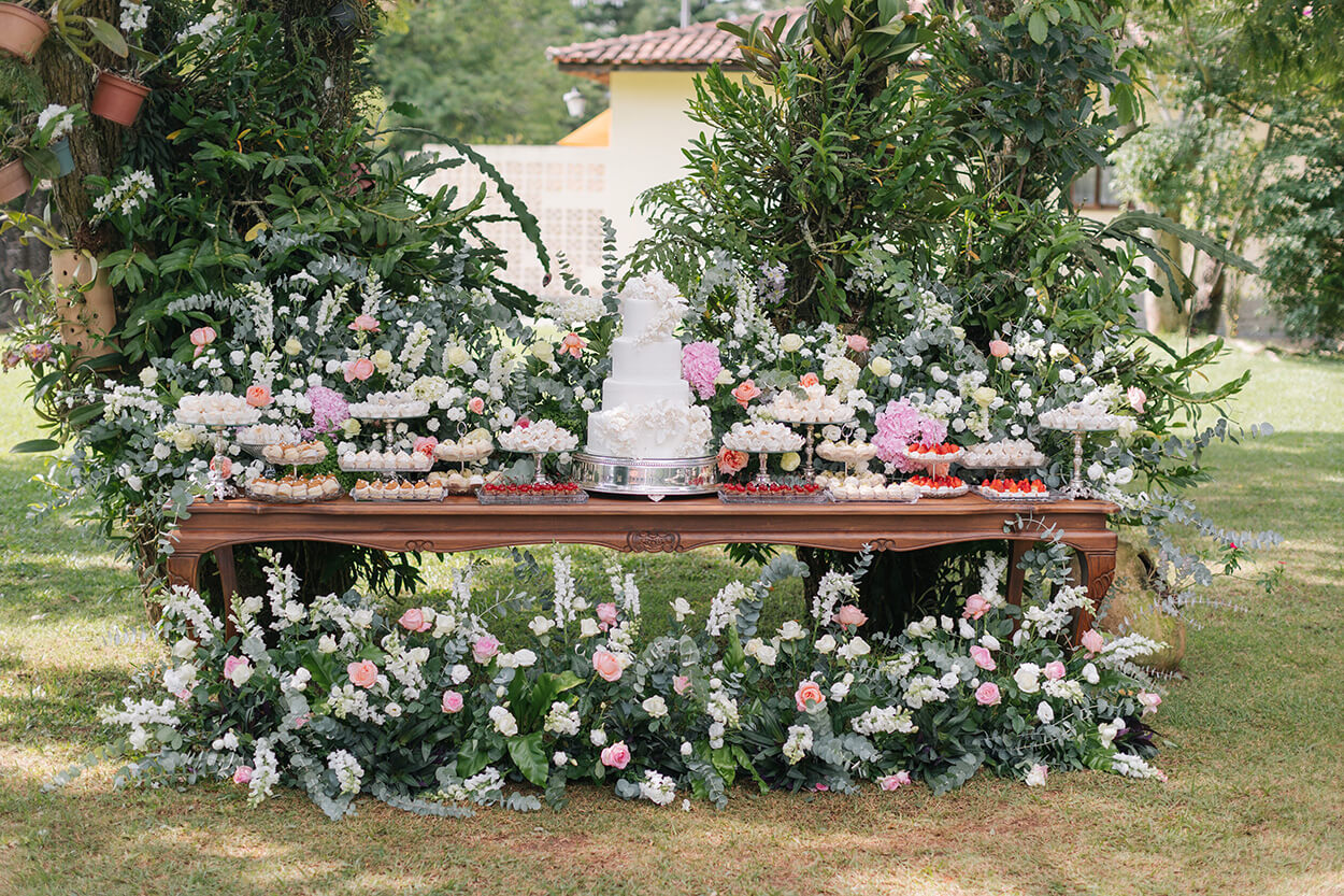 mesa do bolo e bandejas com doces e decorada com rosas brancas e rosas