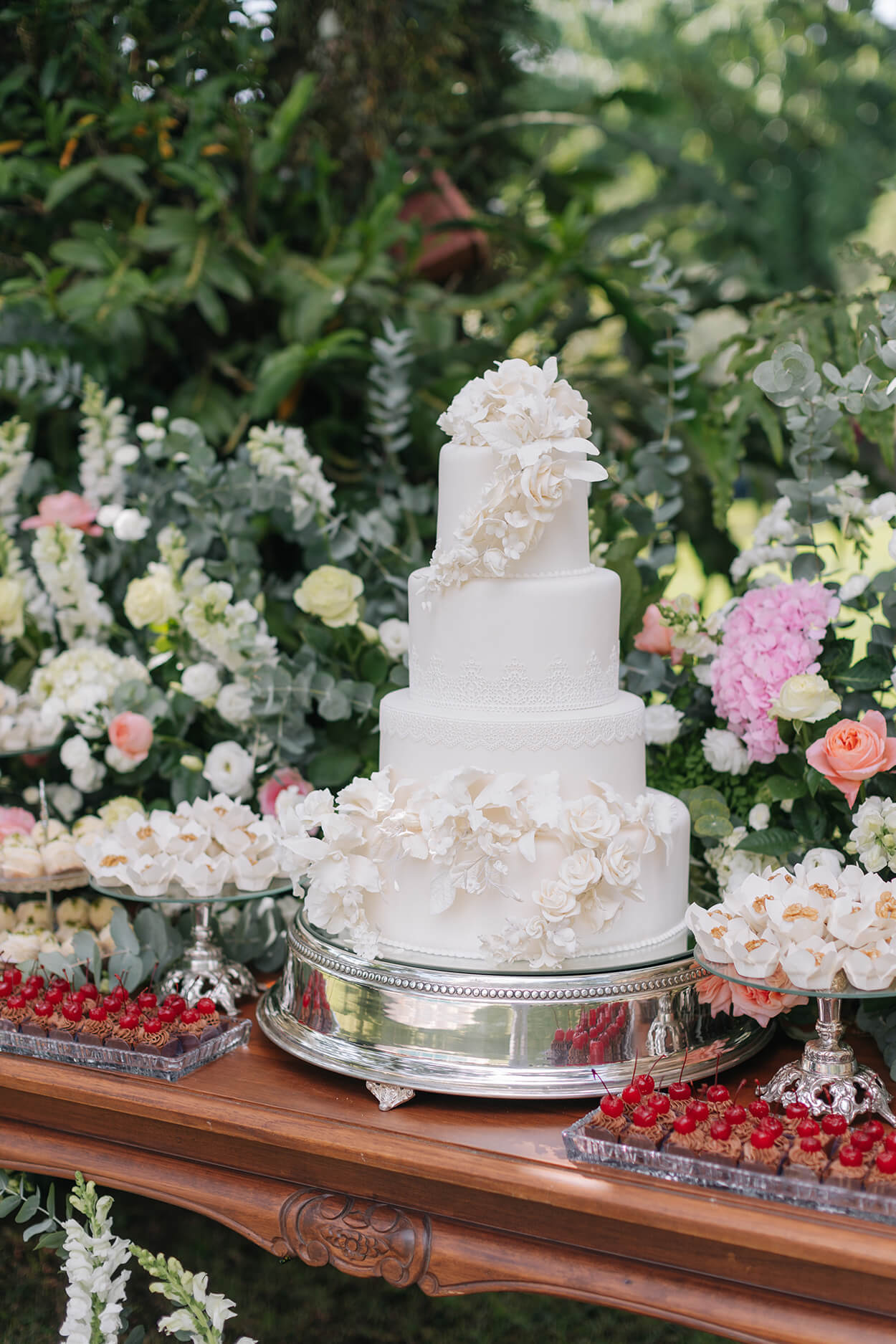 bolo de casamento branco com flores e bandejas com doces e arranjos com flores