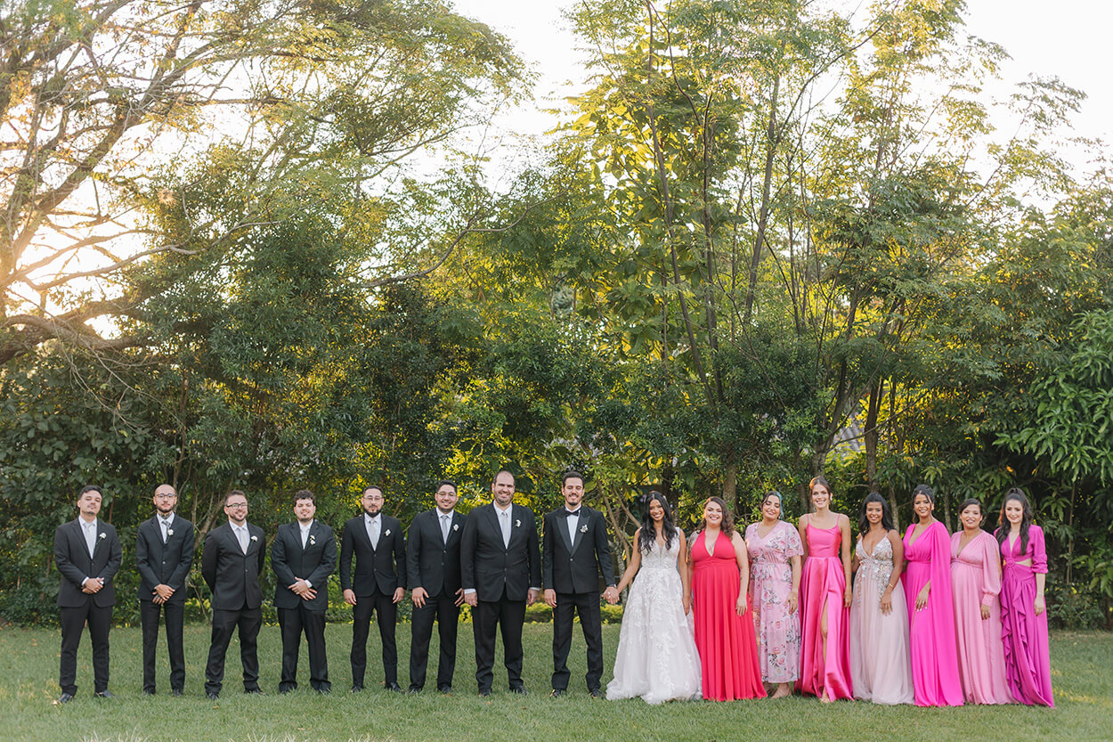 noivos ao lado das madrinhas com vestido cor de rosa e padrinhos de terno preto