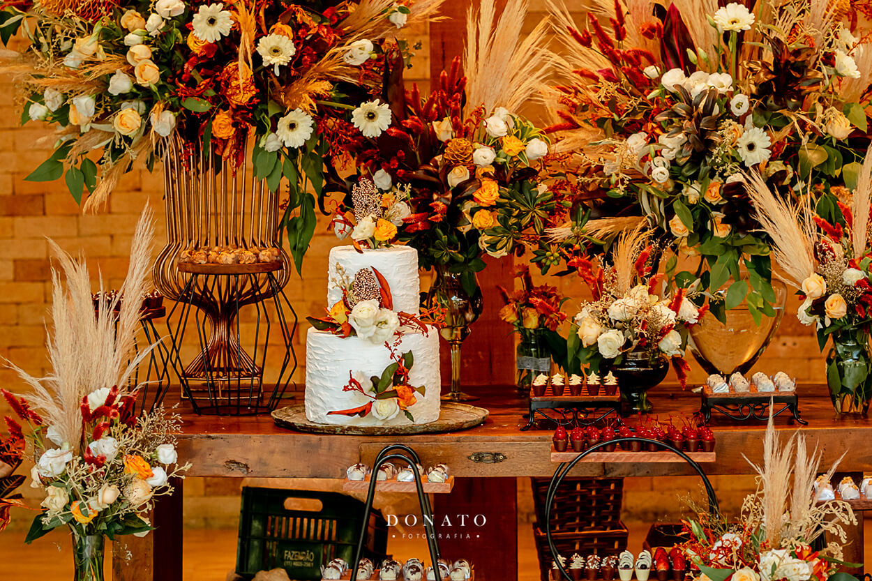 mesa com bolo de casamento e vasos com flores e capim dos pampas