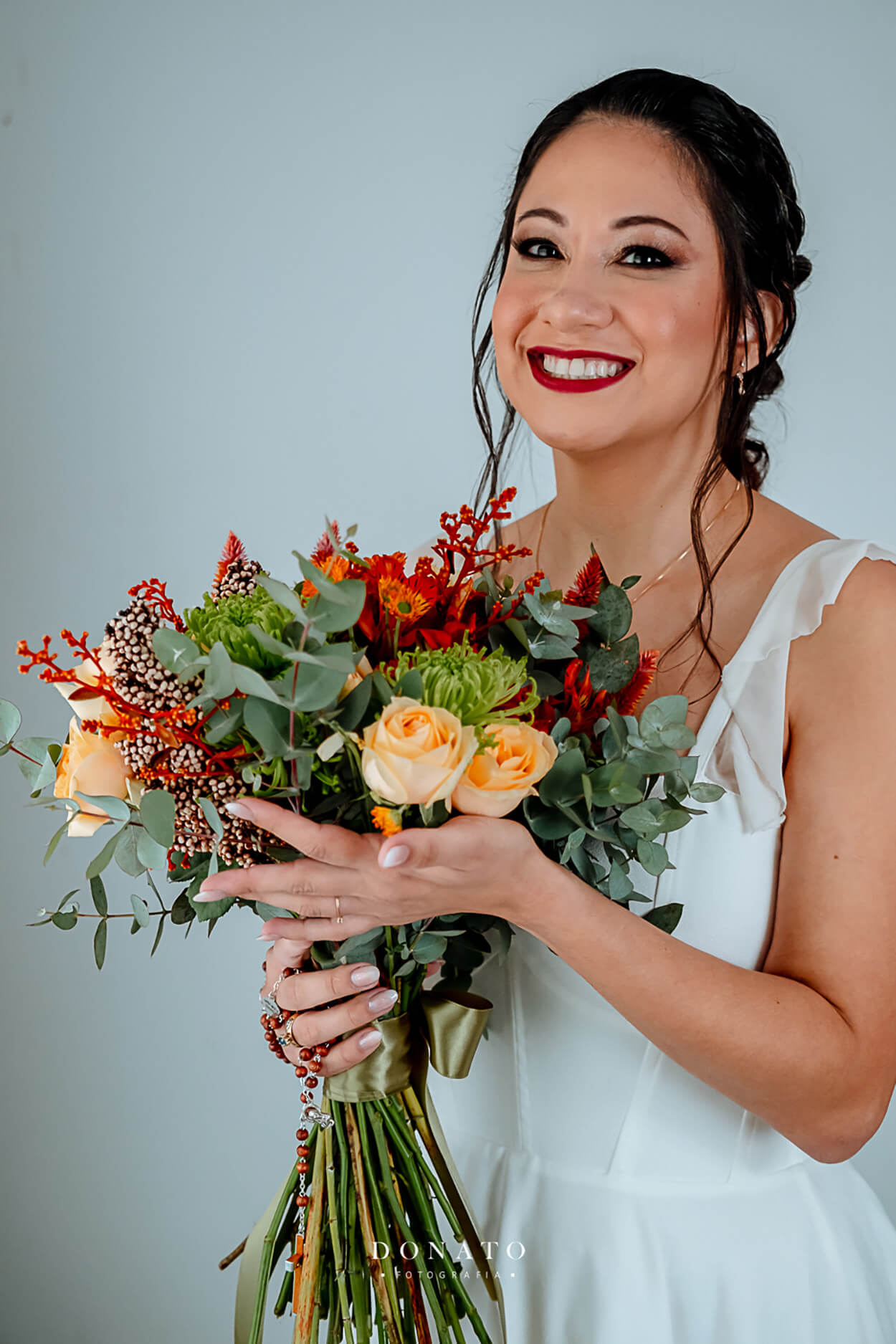 noiva segurando buquÊ com flores vermelhas e rosas laranjas