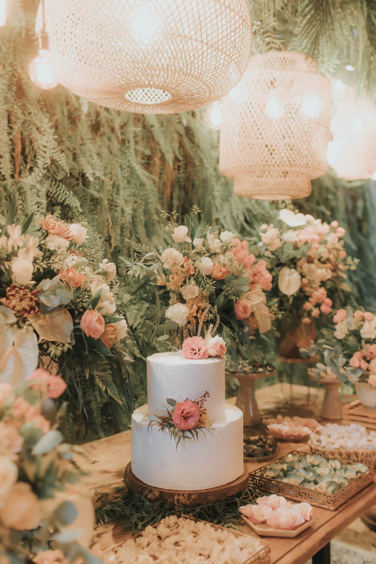 painel com plantas e mesa do bolo com vasos de flores brancas e rosas