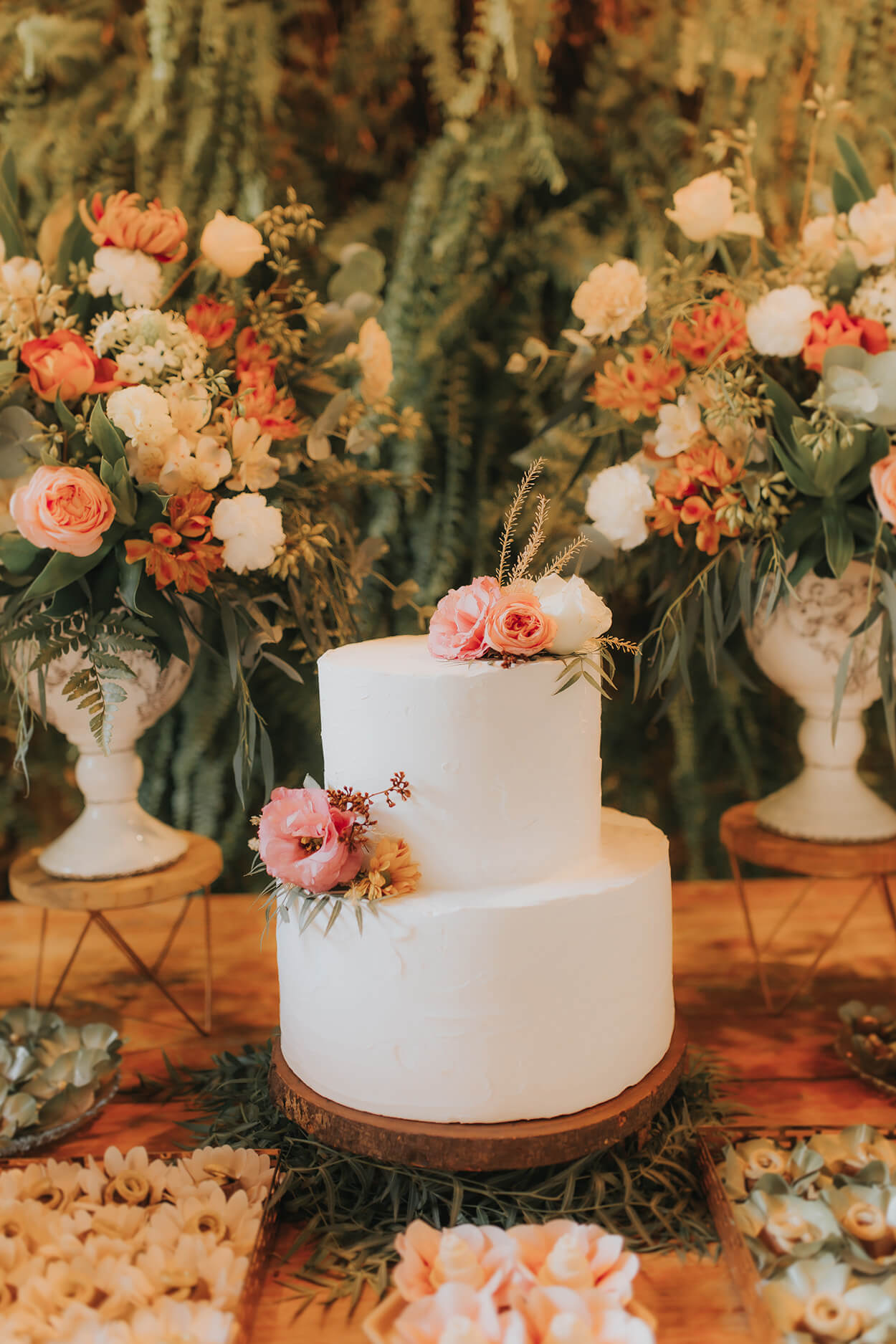 mesa de madeira com bolo de casamento branco com flores rosas brancas e laranjas no topo