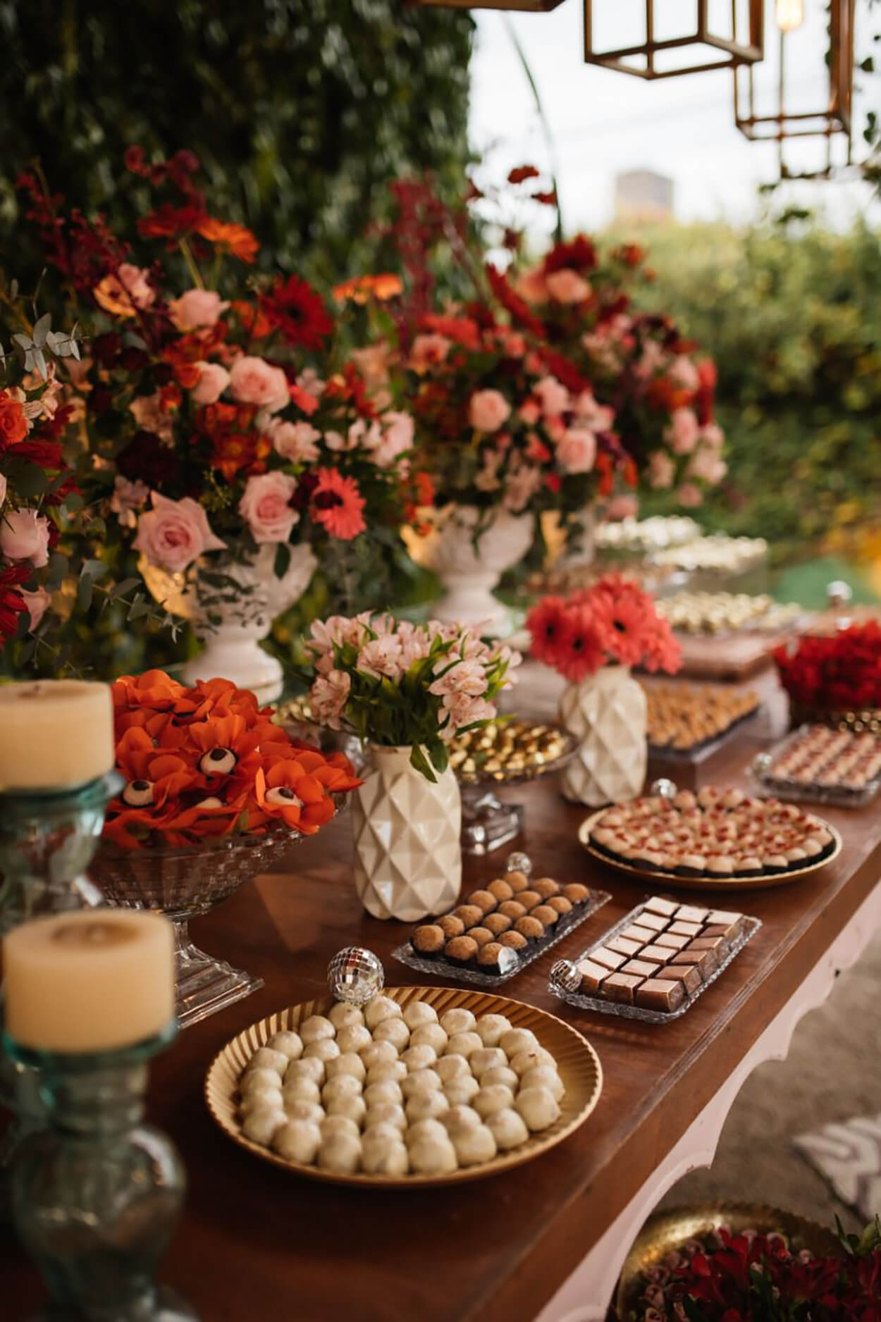 mesa com vasos de flores rosas e bandeja com doces de casamento