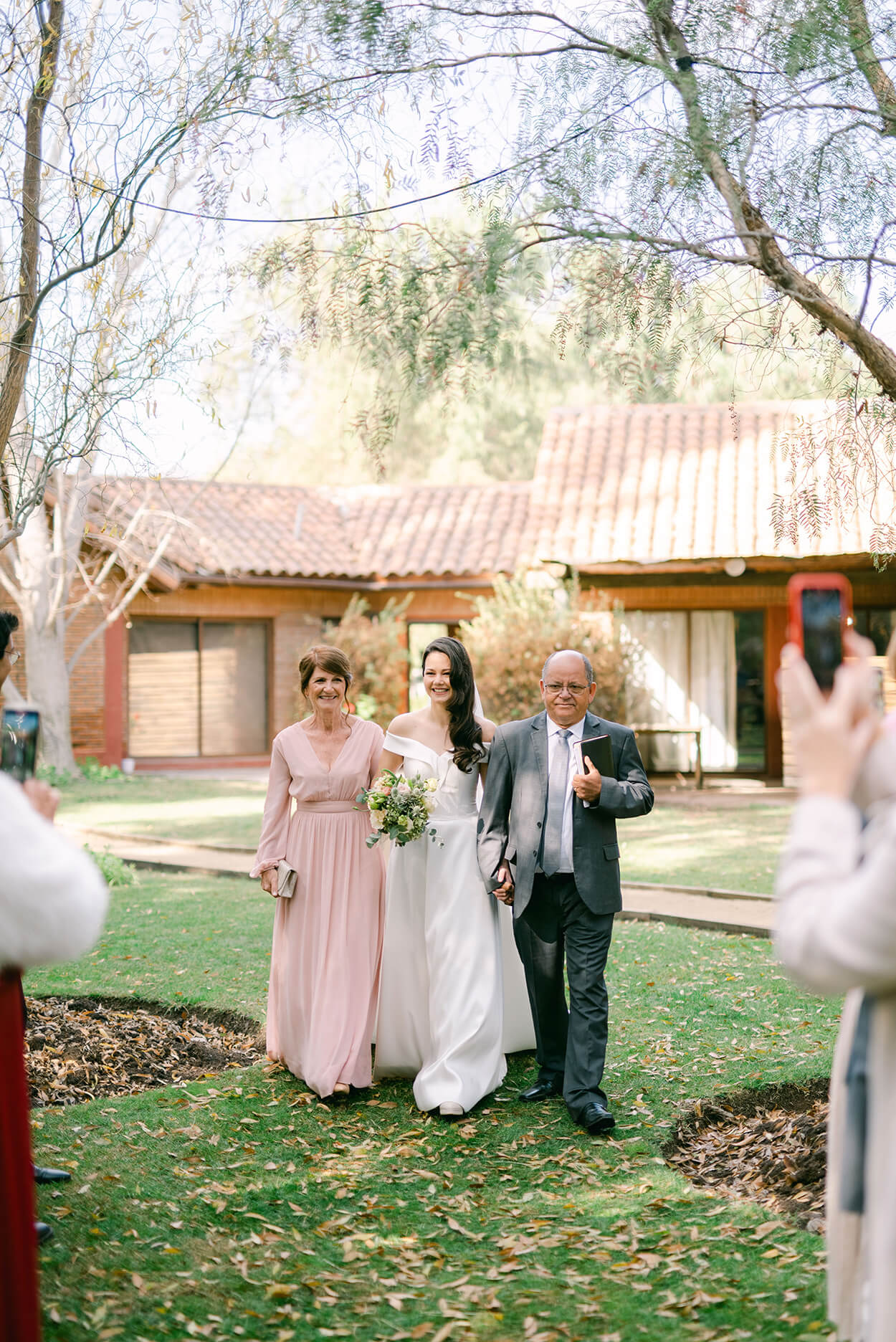 entrada da noiva com a mãe com vestido rosa claro e ao lado do pai com tenro cinza escuro