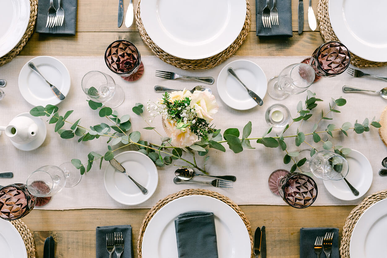 vista de cima de mesa posta com taças marrons e centro de mesa com folhas de eucalipto e rosas brancas