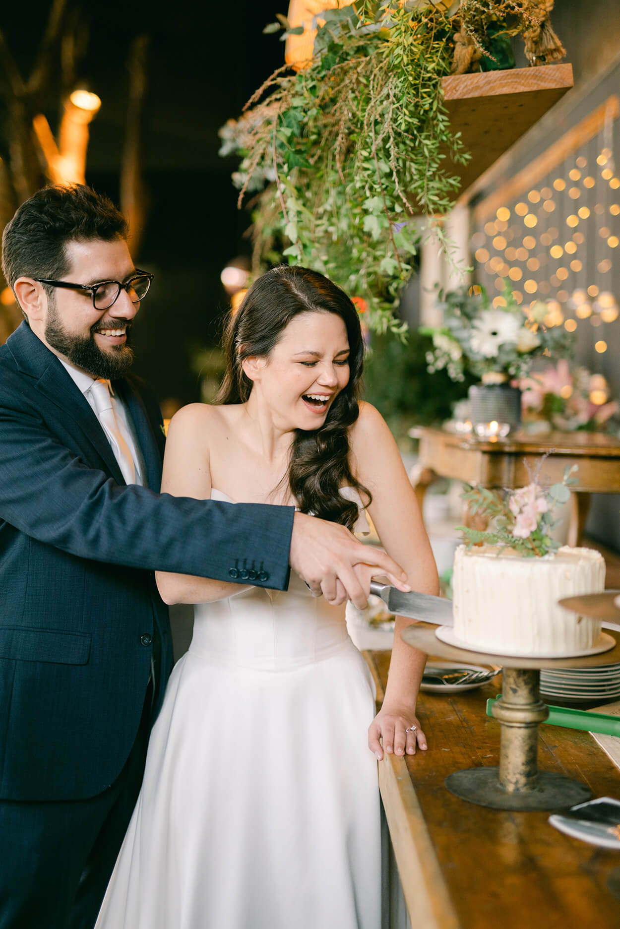 noivos sorrindo enquanto cortam o bolo de casamento