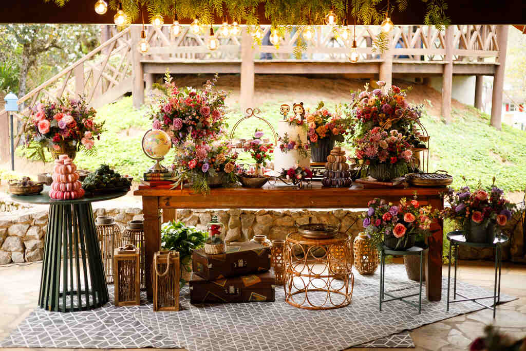salão ao ar livre com mesa de madeira com bolo de casamento com flores rosas e roxas