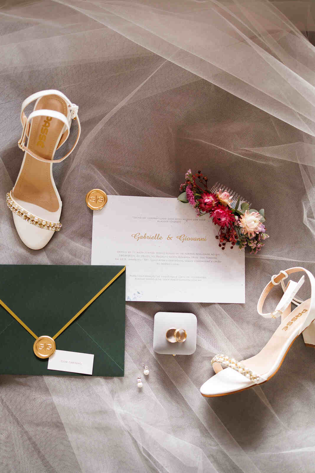 convite de casamento com envelope verde com lacre de cera dourada ao lado de sapato branco sob véu