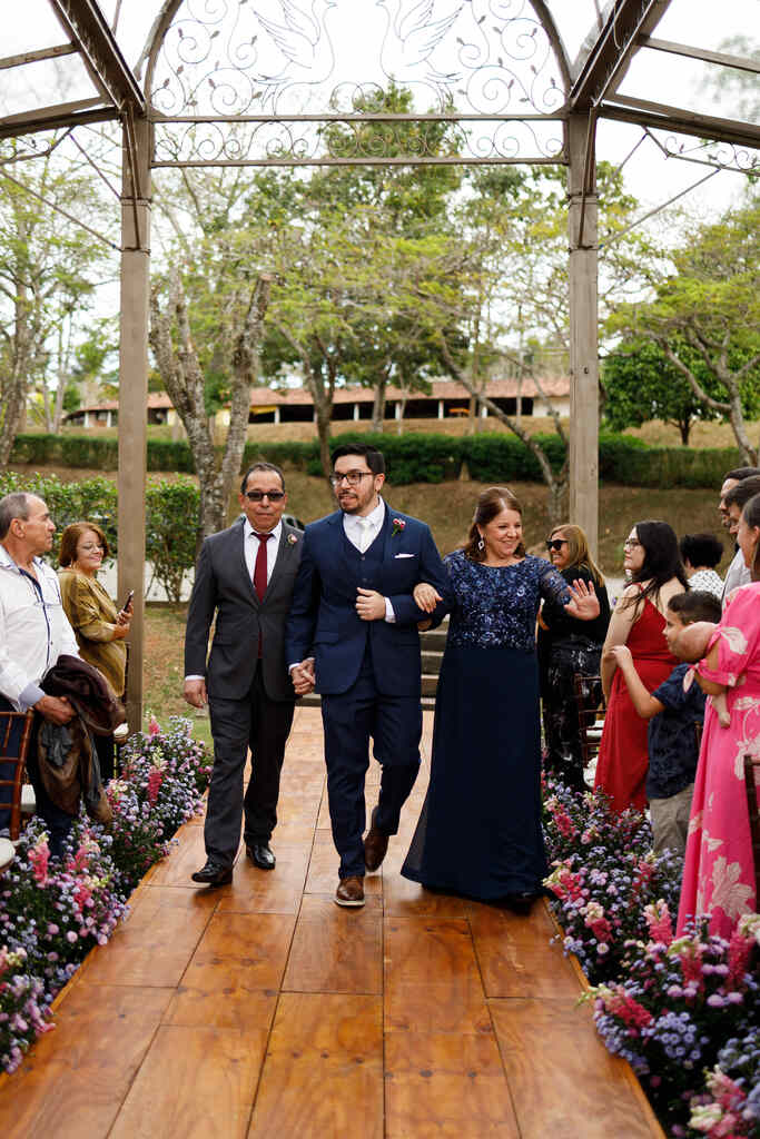entrada do noivo ao lado do pai e mãe com vestidos azul escuro
