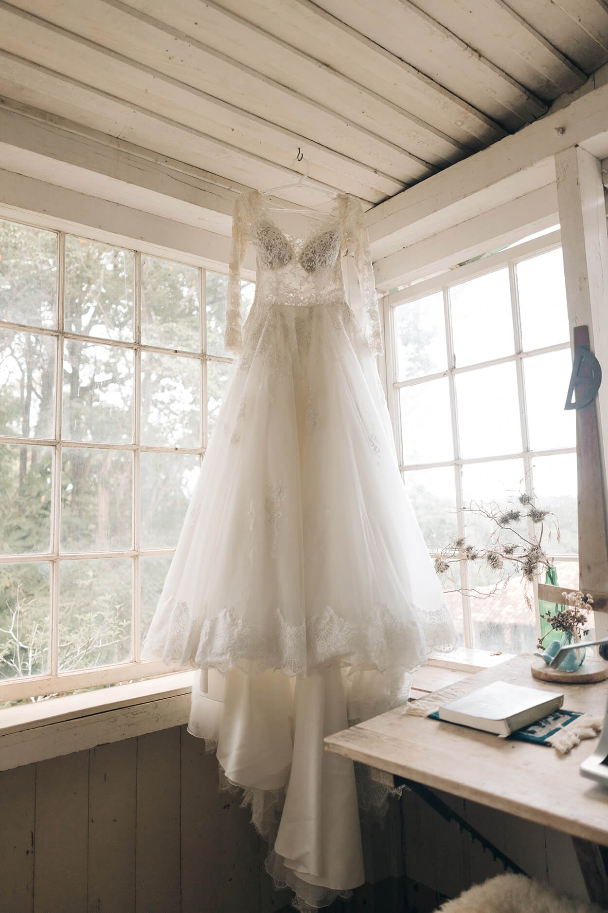Vestido de noiva com mangas pendurado no cabide em frente a janela