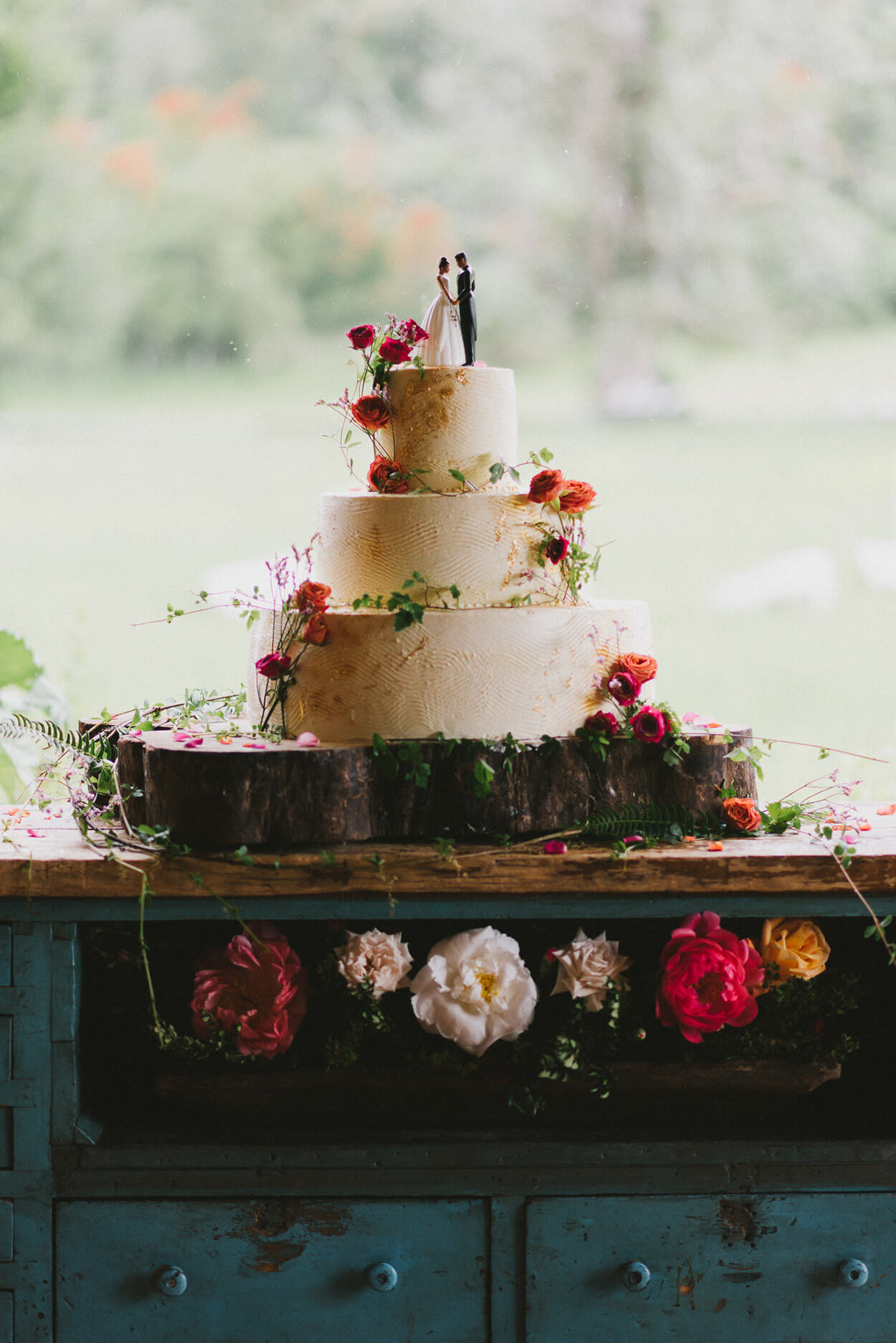 bolo de casamneot branco com três andares com flores rosas e noivos no topo
