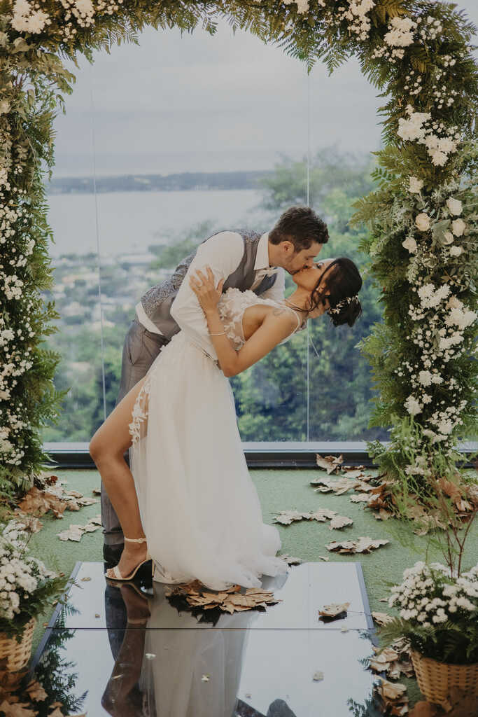  noivos se beijando embaixo de um arco floral T&C Films
