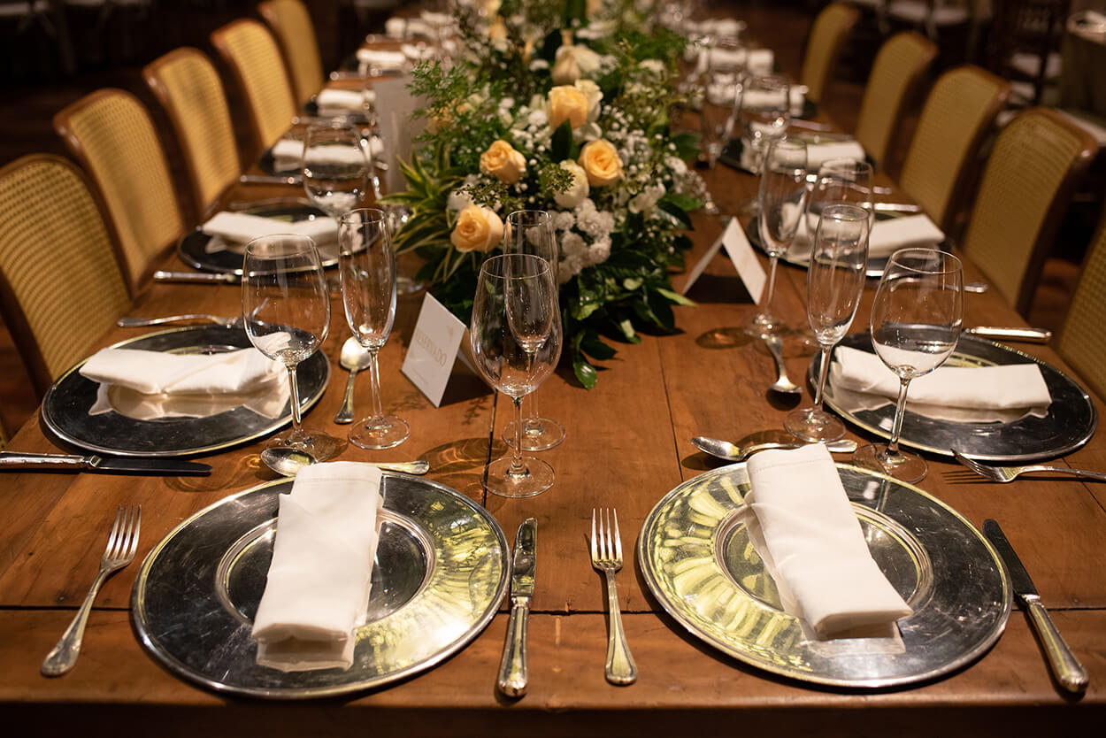 mesa comunitária para casamento com sousplat d eprata e flores brancas e laranjas no centro