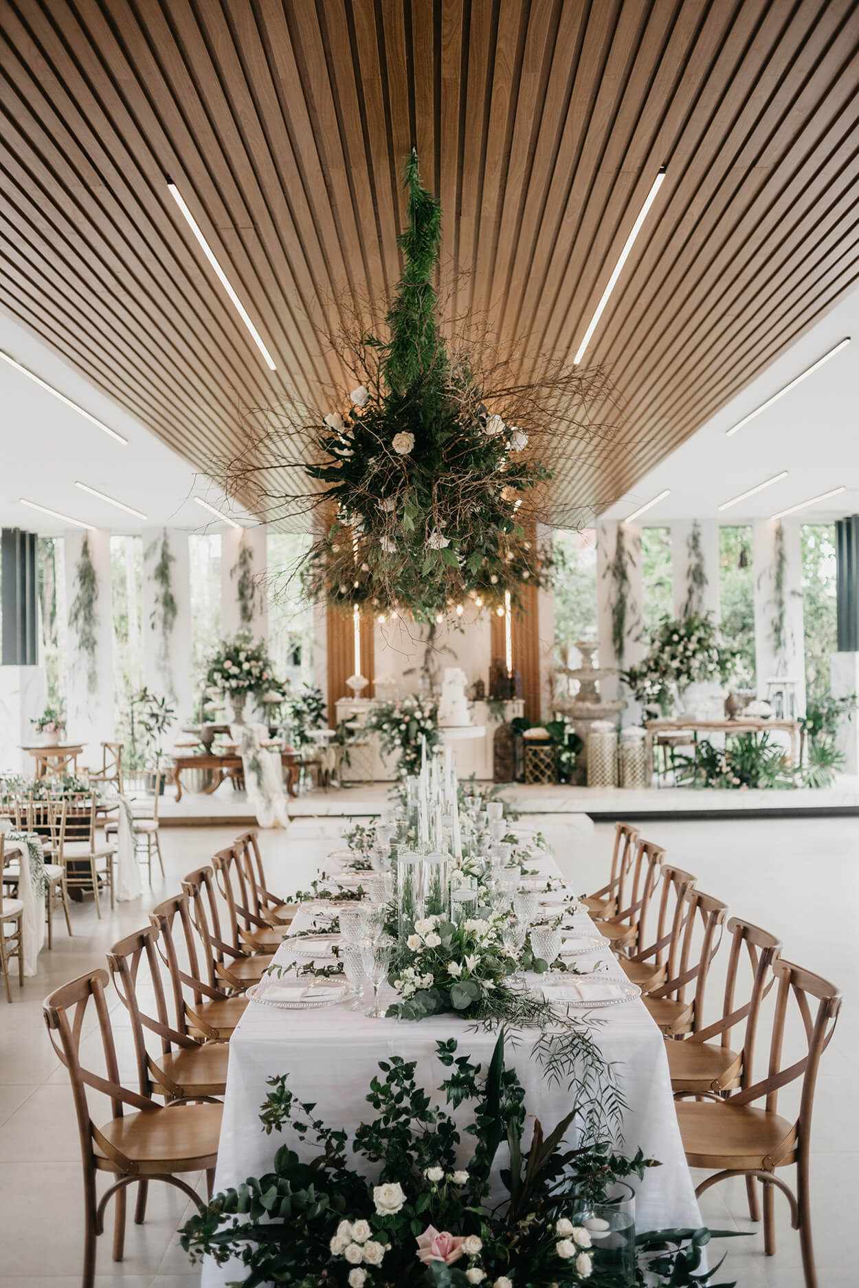 salão com mesa retangular posta com toalha branca flores brancas e flroes supensas no teto