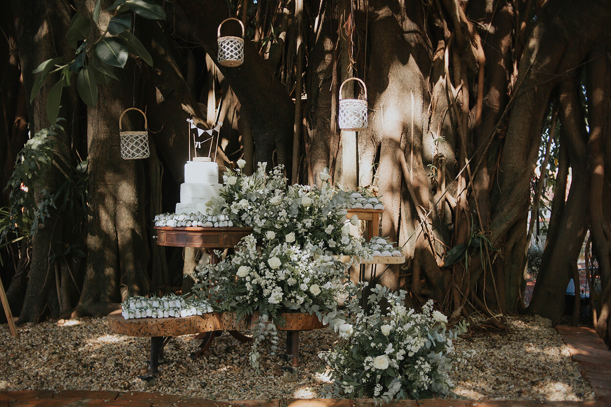 mesas de madeira com arranjos de flores brancas e bolo de casamento 