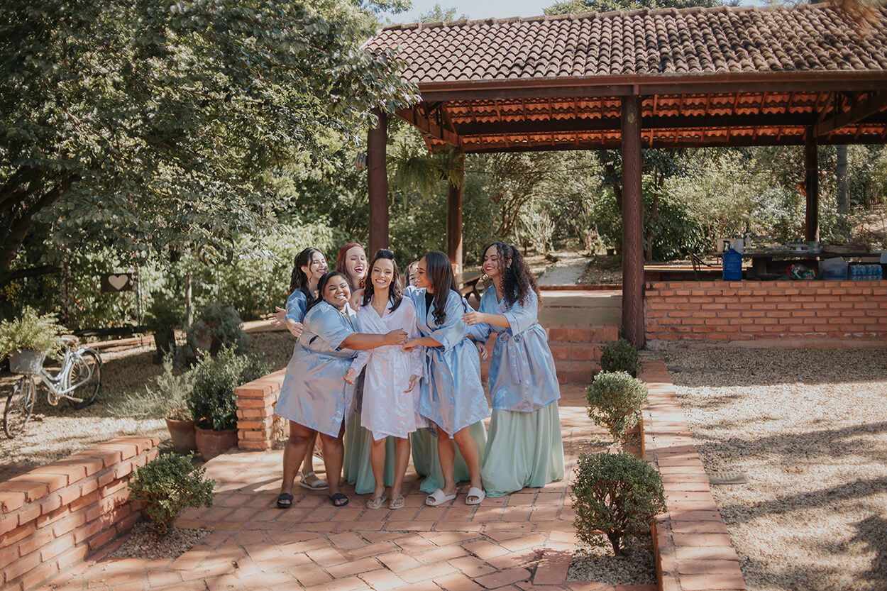noiva com robe branco e madrinhas com robes azuis claros no campo