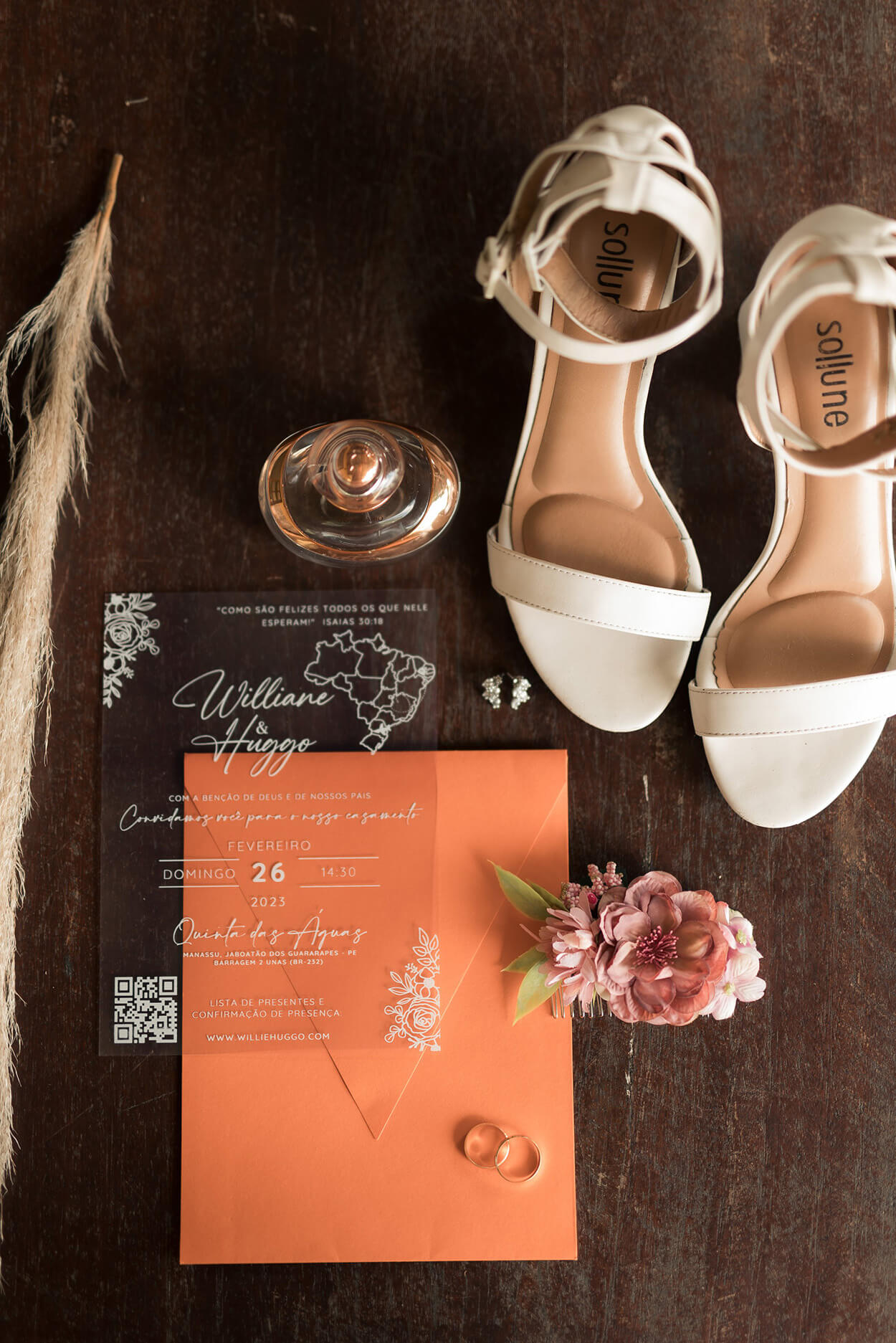 convite de casamento transparente ao lado de sandália branca e perfume em cima da mesa