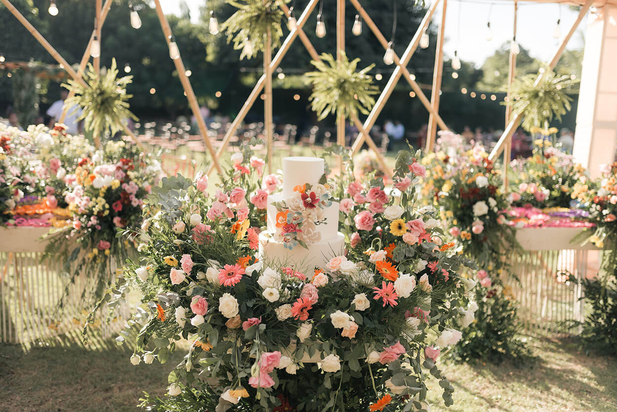 mesa cheia de flores brancas rosas e laranja com bolo de casamento
