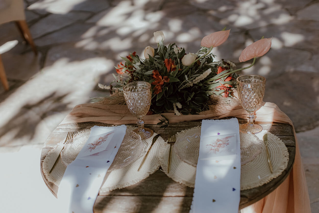 mesa de madeira redonda dos noivos com susplat de vidro taças transparentes e flores brancas rosas e laranjas no centro