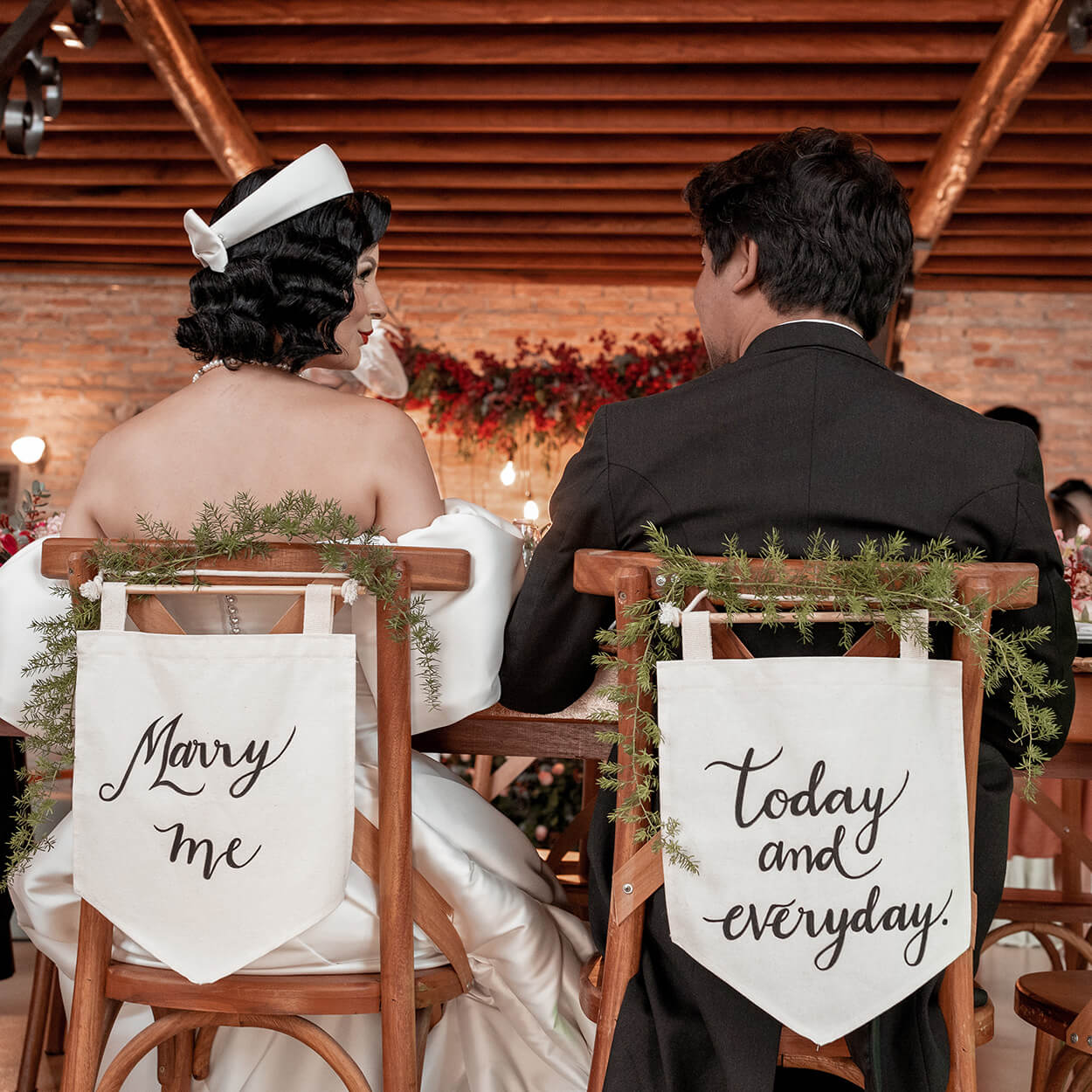 noivos sentados em cadeiras com flâmulas escrito marry me today and everyday