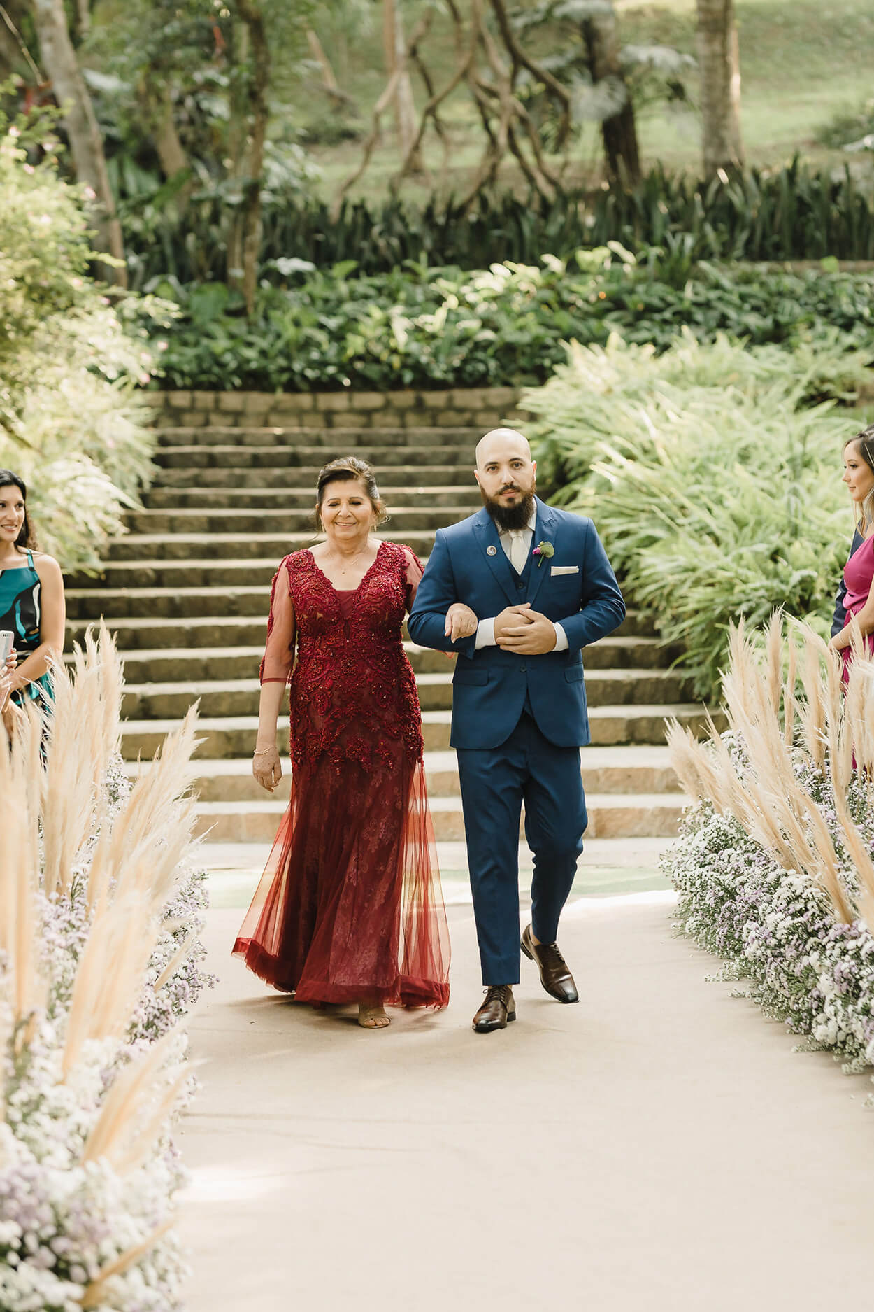 entrada do noivo com tenro azul ao lado da mãe com vestido longo vermelho
