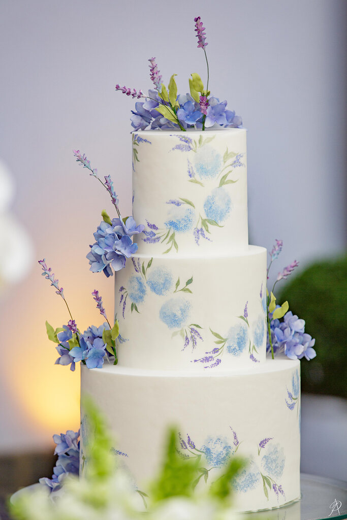 bolo de casamneto branco de três andares com flores azuis e lavandas no topo e flores estampadas no bolo
