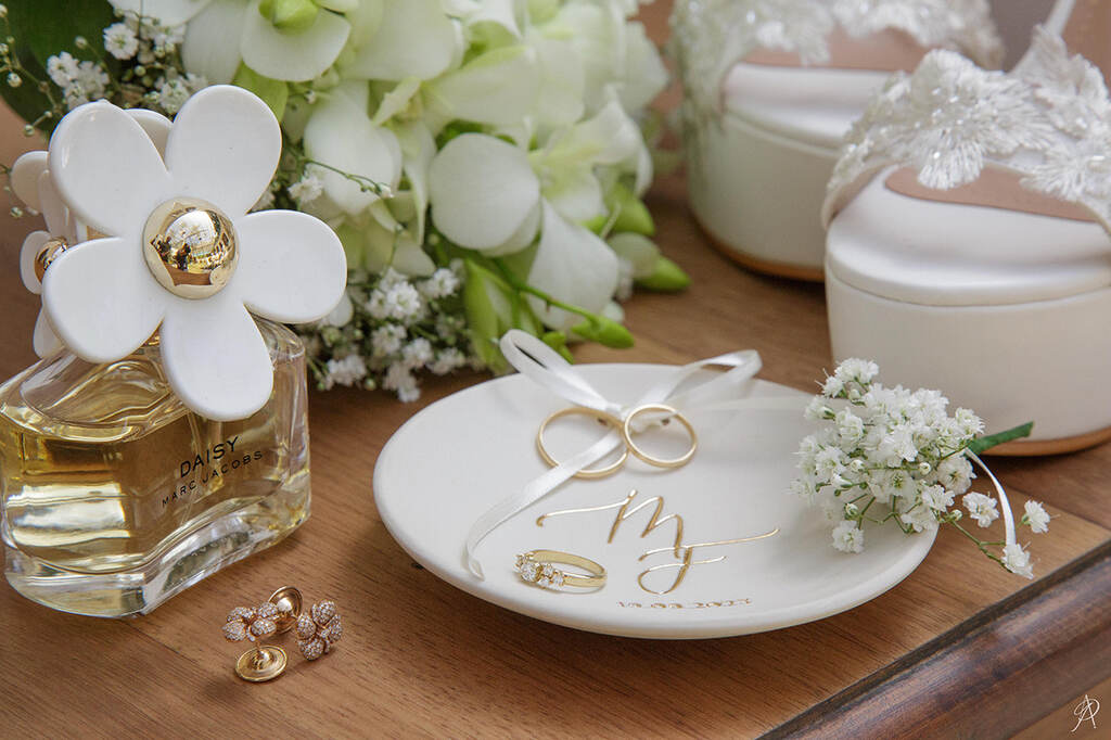 prato de porcelana com iniciais em dourado para porta alianças ao lado de perfume e flores