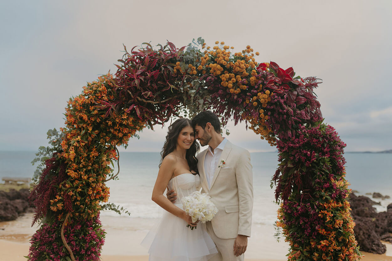 noivos abraçados no altar florido com flores rosas e laranjas de frente para o mar