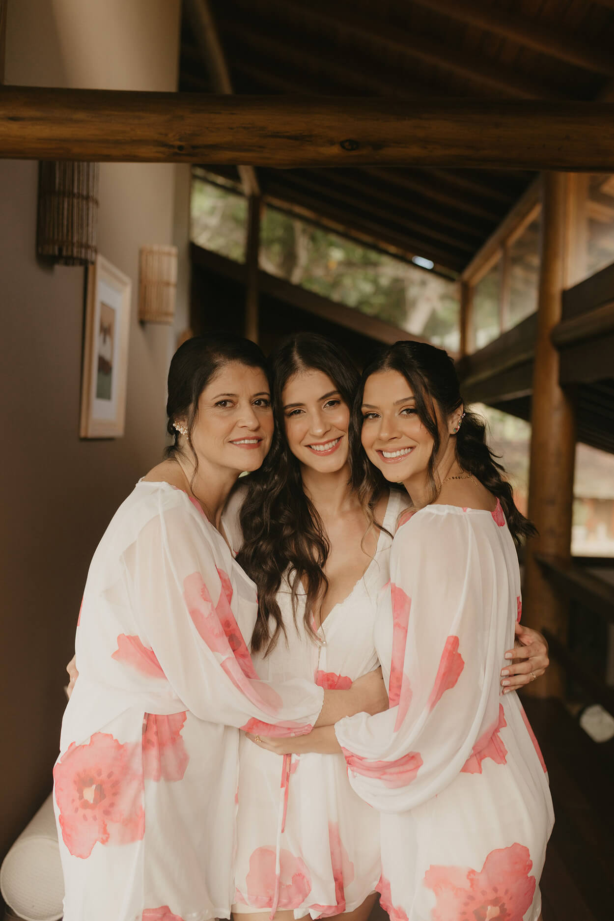 noiva abraçando mais duas mulheres com robe branco com flores cor de rosa
