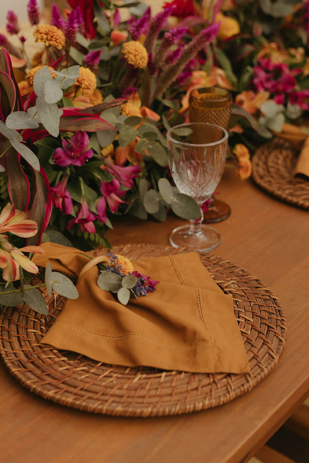 mesa posta com sousplat de palaha com guardanapo marrom e flores laranjas e rosas no centro
