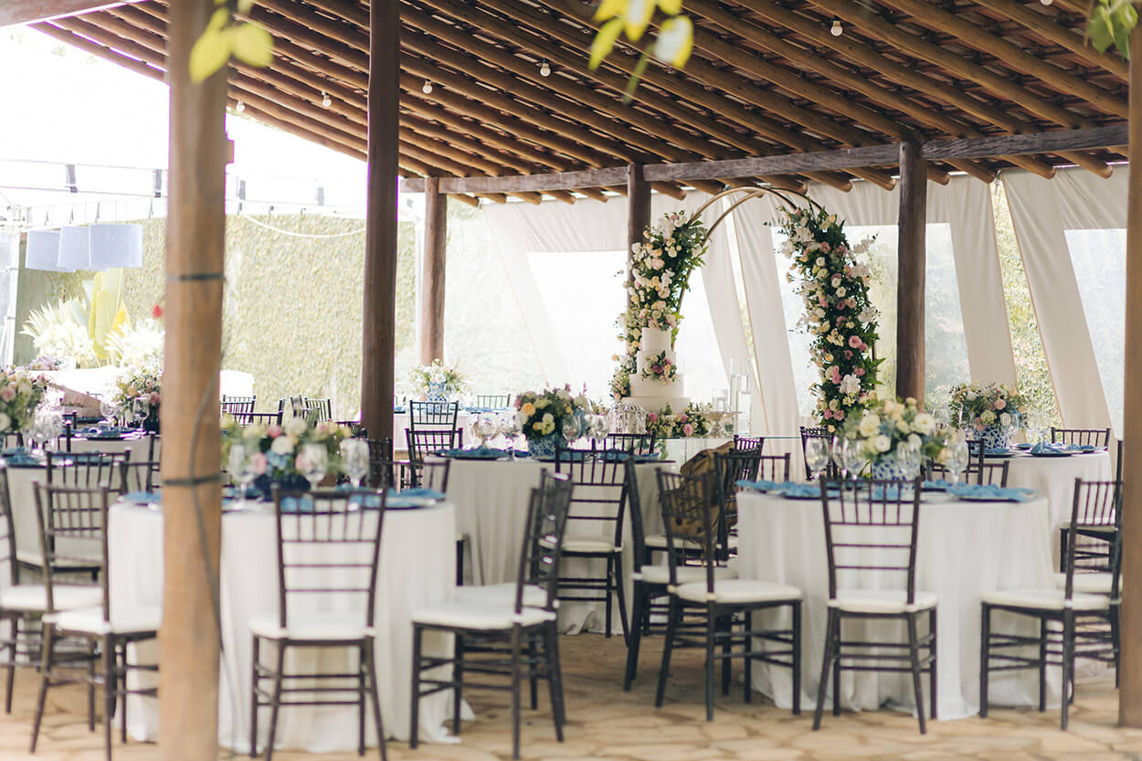 salão coberto ao ar livre com mesas redondas com toalha branca e mesa posta azul