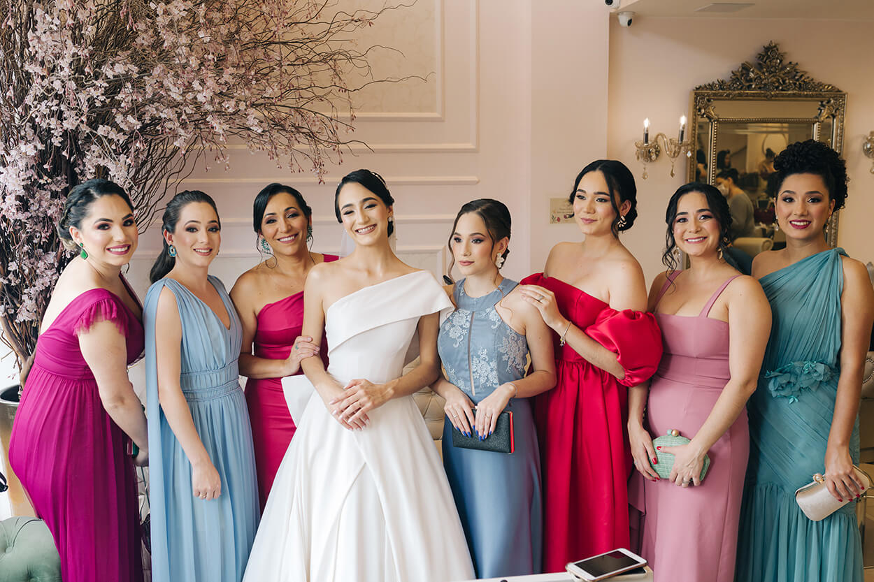 noiva ao centro e madrinhas com vestidos rosas e azuis dentro de sala cor de rosa