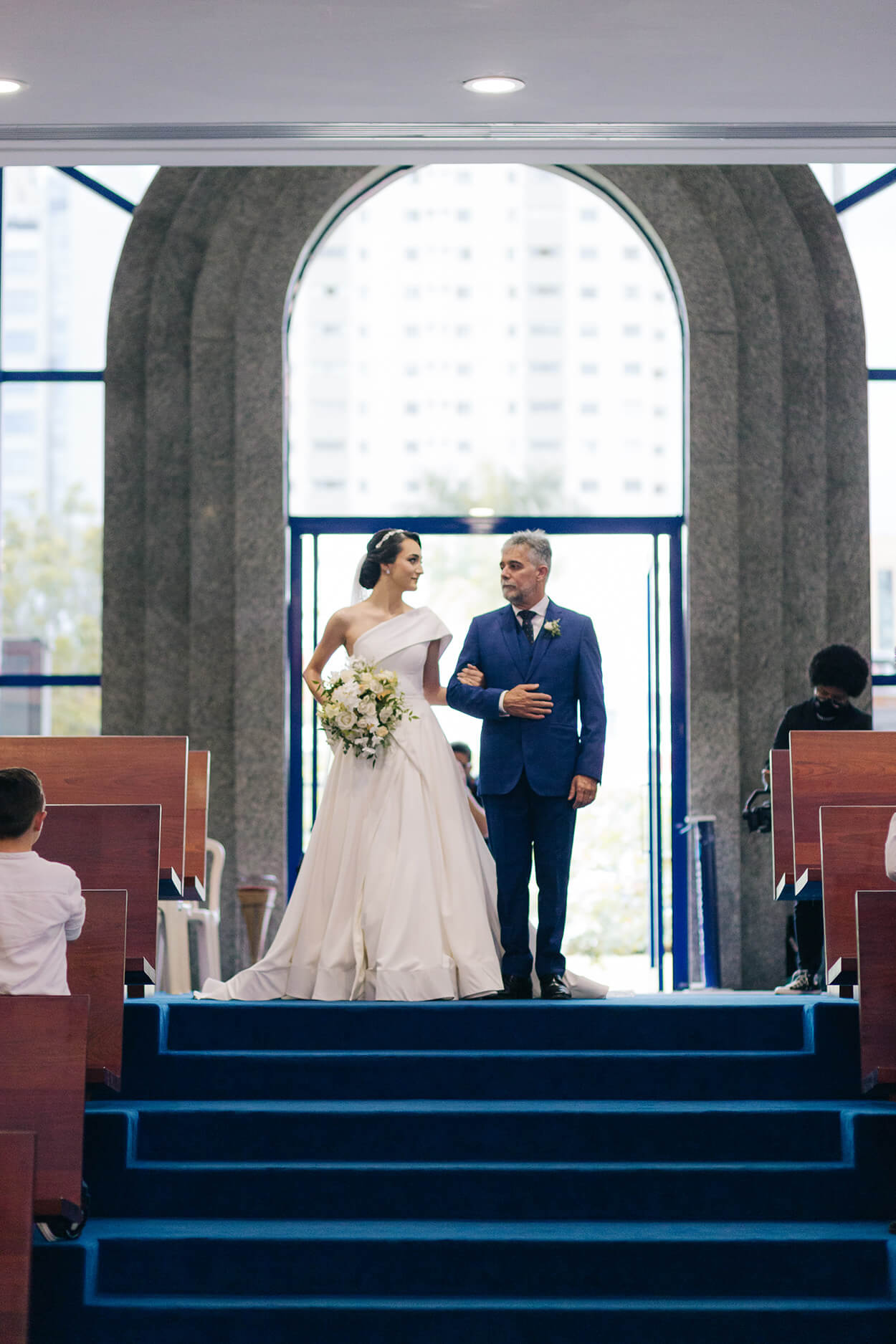 entrada da noiva segurando o buquÊ na igreja ao laod do pai com tenro azul