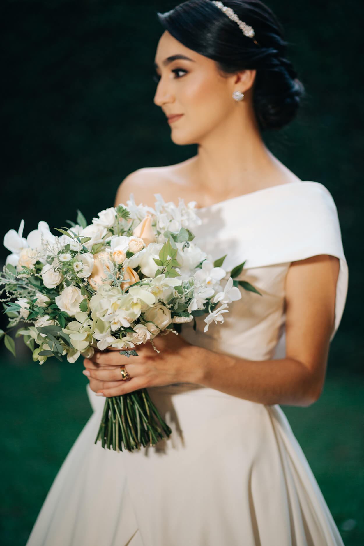 noiva segurando buquê redondo com flores brancas e vestido com ombro único