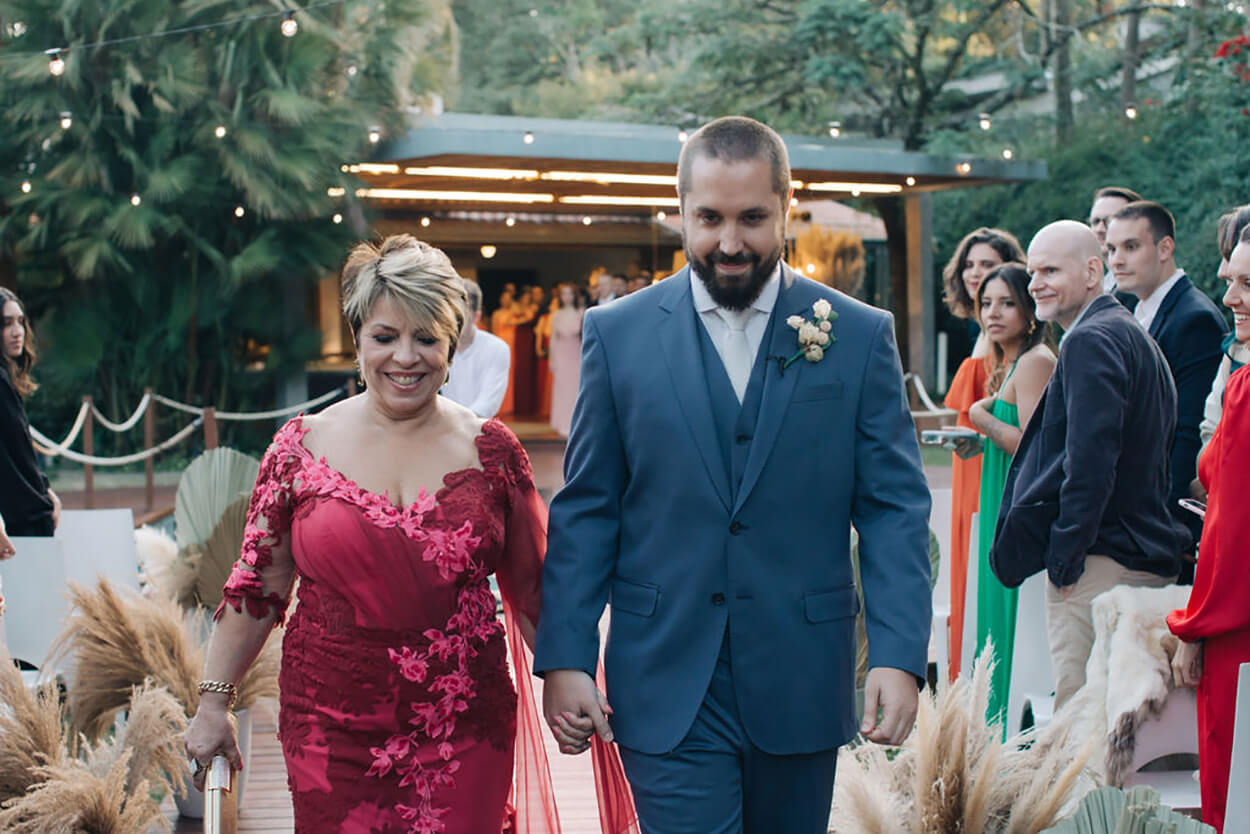 entrada do noivo com terno azul ao lado da mãe com vestido rosa