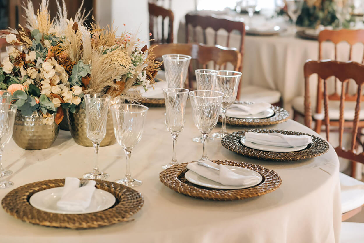 mesa redonda com toalha branca com mesa posta com sousplat rustico