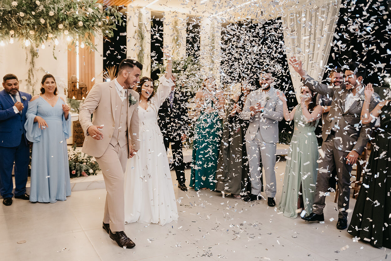 saída dos noivos comemorando enquanto convidados ogam confetes brancos