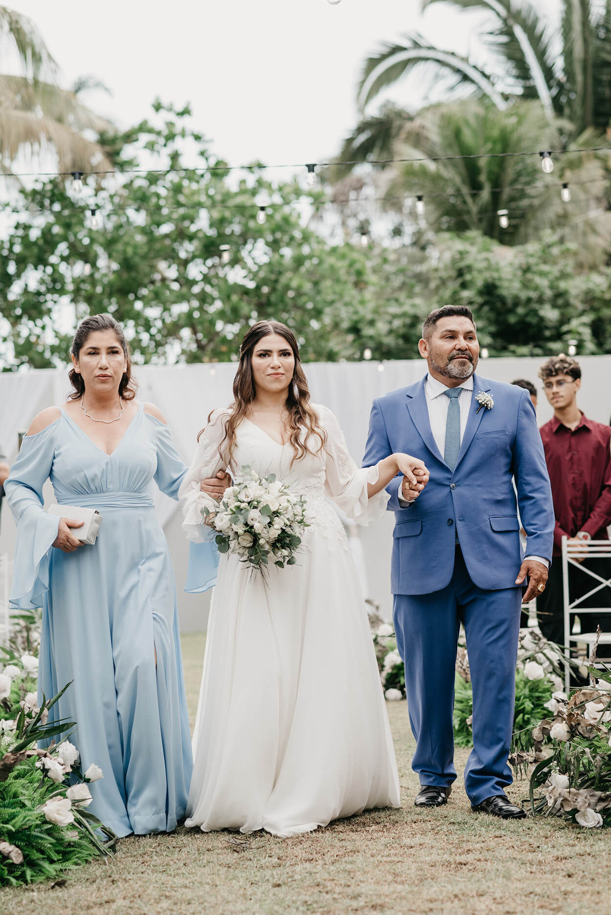 entrada da noiva com a mãe com vestido longo de mangas azul serenity e pai com terno azul
