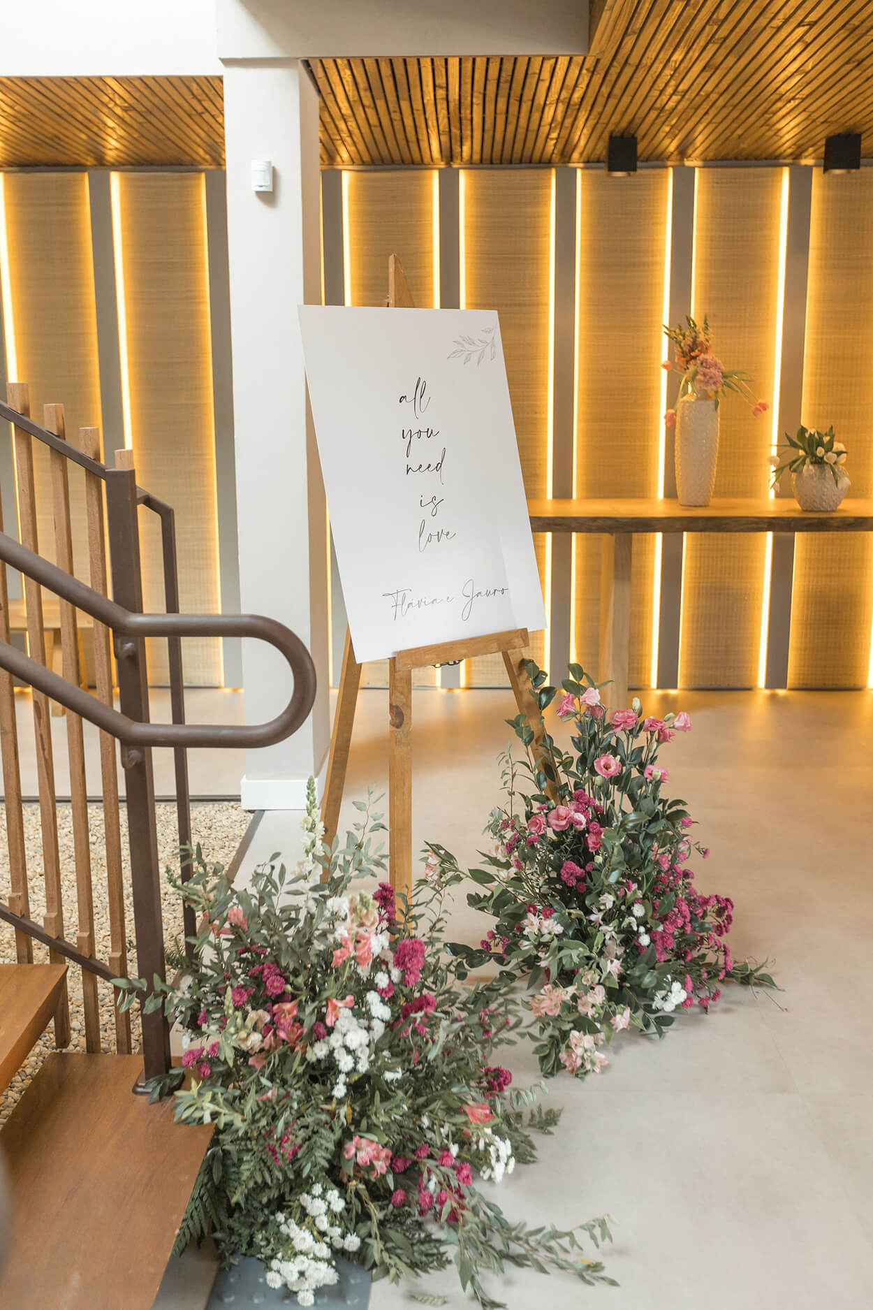 cavalete com quadro branco escirto o nome dos noivos enfeitado com flores brancas e rosas no chão e na escada
