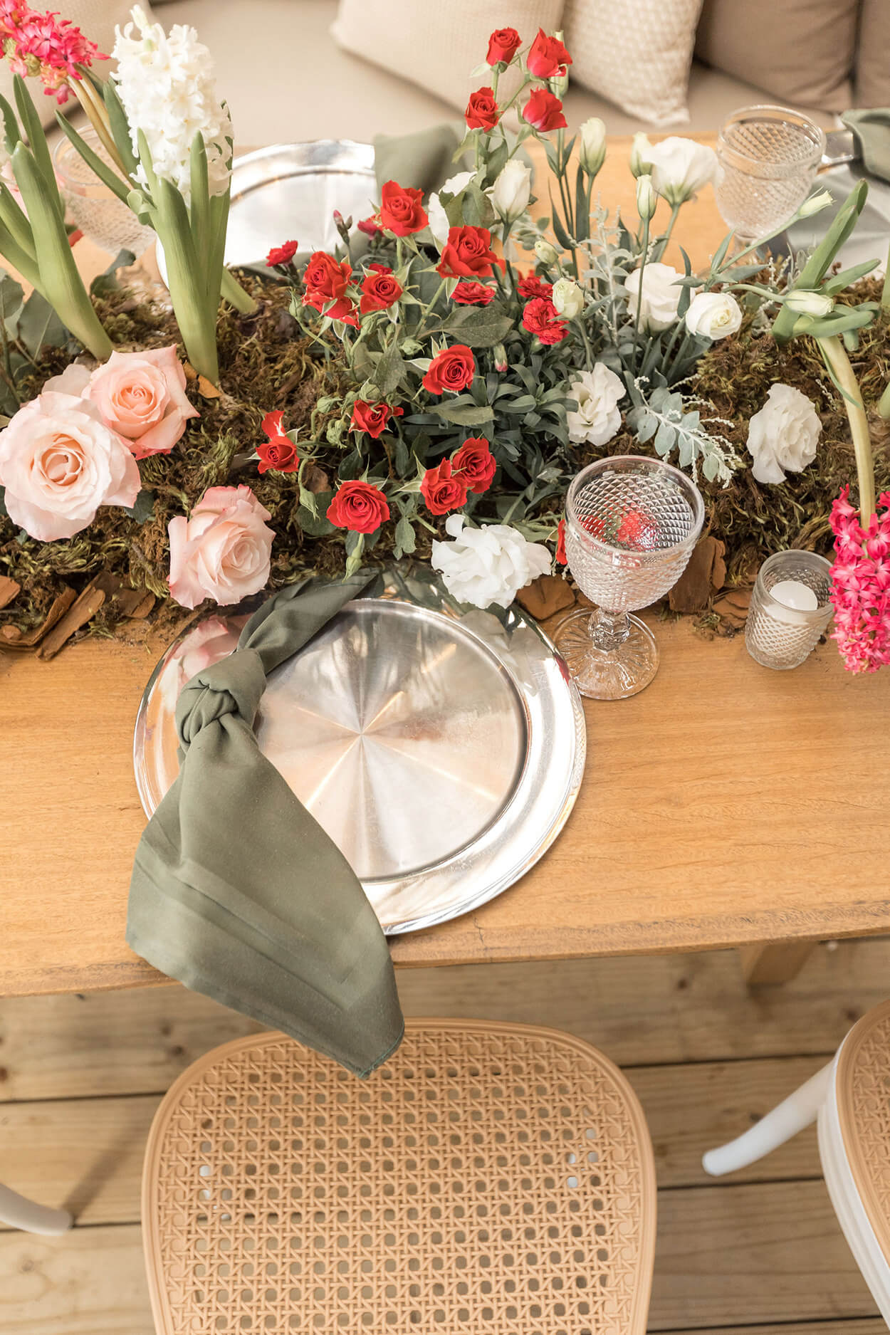 mesa posta com sousplat prateado com guardanapo verde e flores rosas vermelhas e brancas no centro da mesa