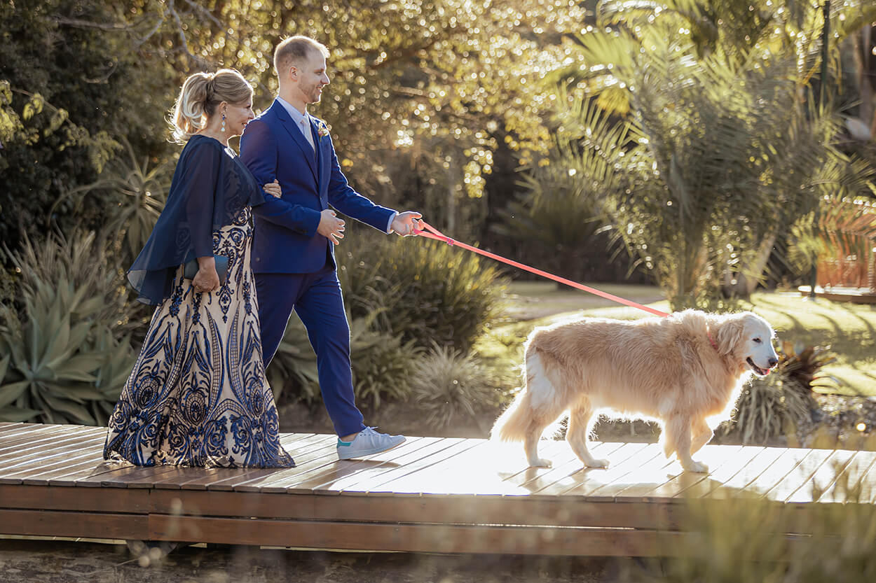 entrada da noiva com terno azul levando cachorro golden retriever na ponte com a mãe usando vestido branco e azul estampado