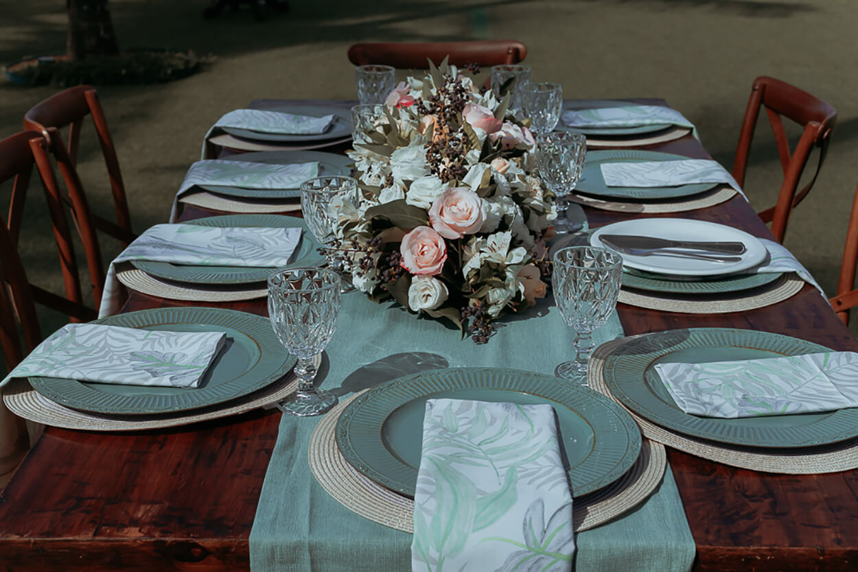mesa posta com guardanapos verdes e flores brancas e rosas no centro