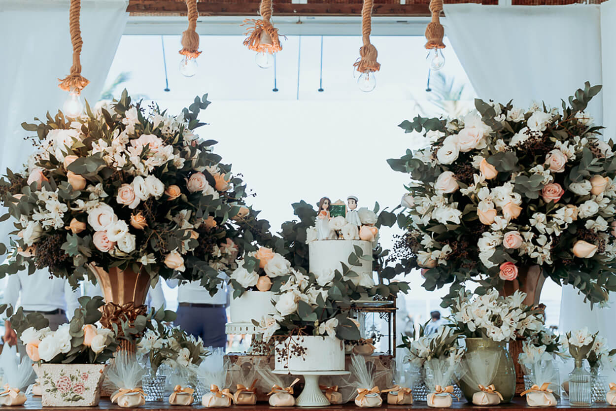 mesa com trio de bolos de casamento com dois vasos grandes com flores brancas rosas e laranjas 