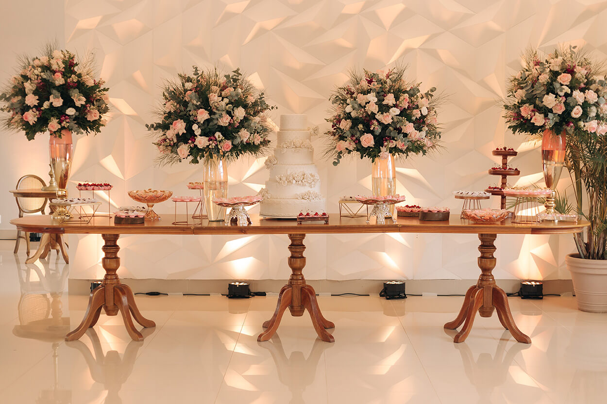 mesa de madeira com bolo de casamento branco com 4 andares com flores e arranjos com rosas brancas e cor de rosa